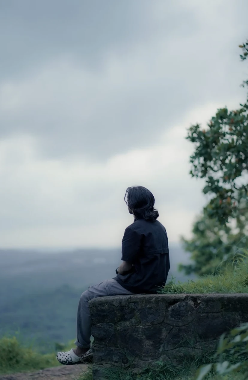 Pose reference of a person sitting on a stone wall facing a landscape